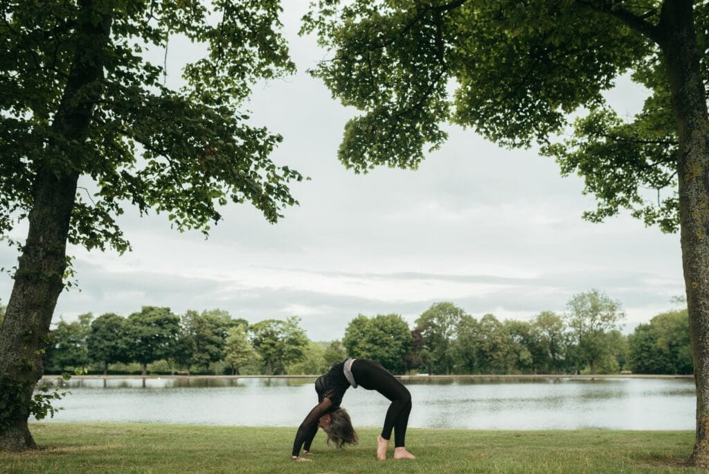 Side view of anonymous slim lady in sportswear standing in Urdhva Dhanurasana pose while practicing yoga on river shore