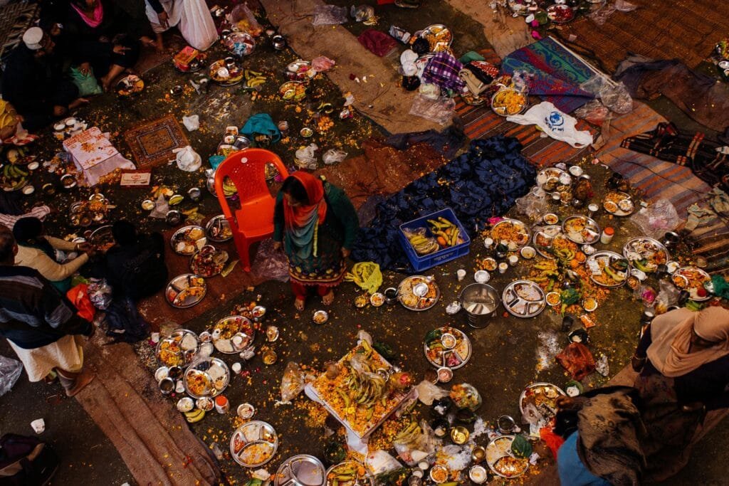 Overhead shot of people gathered with scattered plates of food outdoors, reflecting cultural event.
