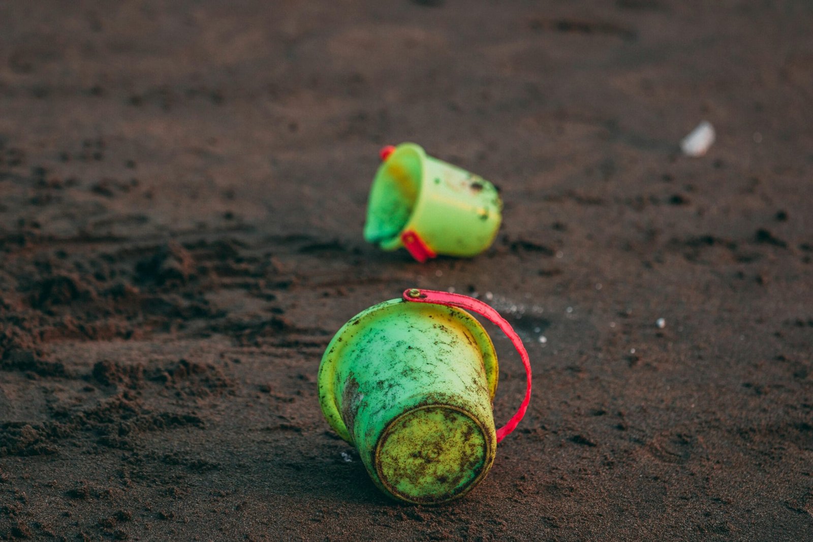 Bright green plastic buckets scattered on a sandy beach, capturing a playful seaside scene.